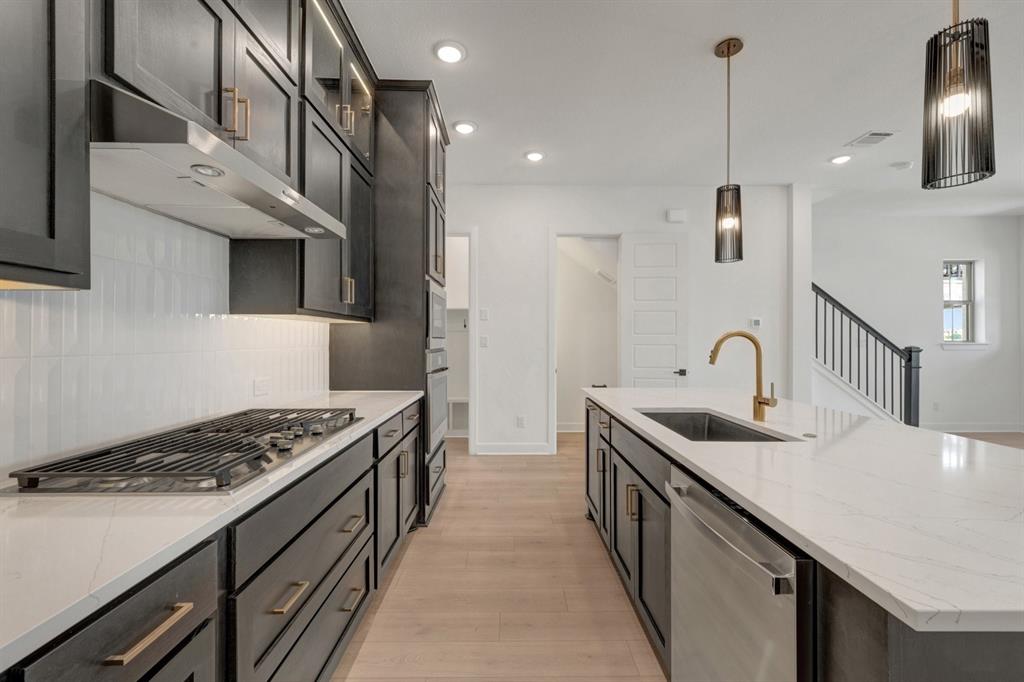 Modern kitchen featuring a gas cooktop, stainless steel hood, quartz countertops, a large island with an undermount sink, and dark cabinetry with brass hardware