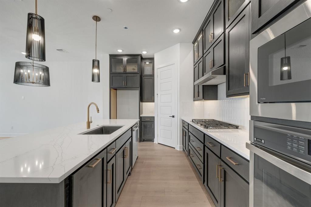 Gourmet kitchen featuring an oversized island with an undermount sink and gold-finish faucet, dark cabinetry, and light wood-finish flooring