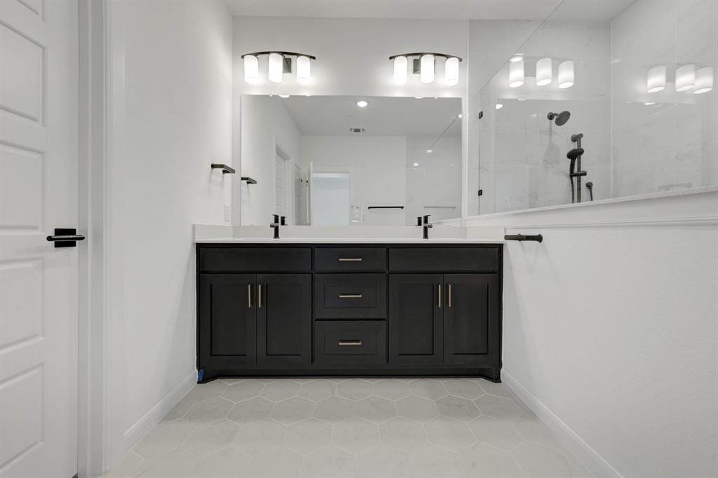 Dual vanity with black cabinetry, white countertops, hexagon tile flooring, and a glass-enclosed shower with black fixtures