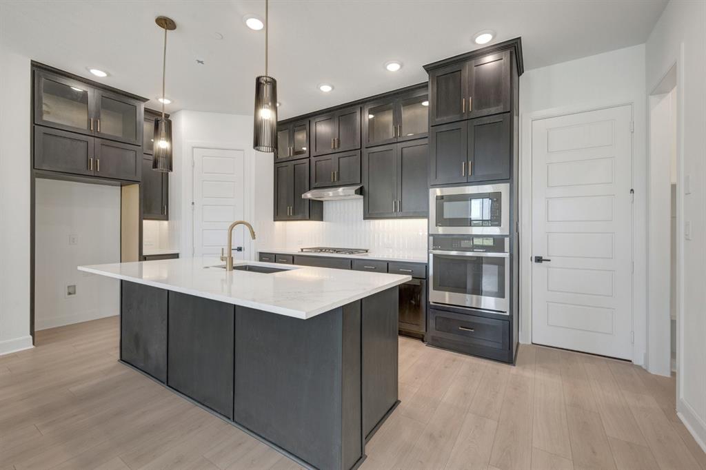 Kitchen featuring a spacious island with a white countertop, dark cabinetry, stainless steel appliances, and wood-finish flooring