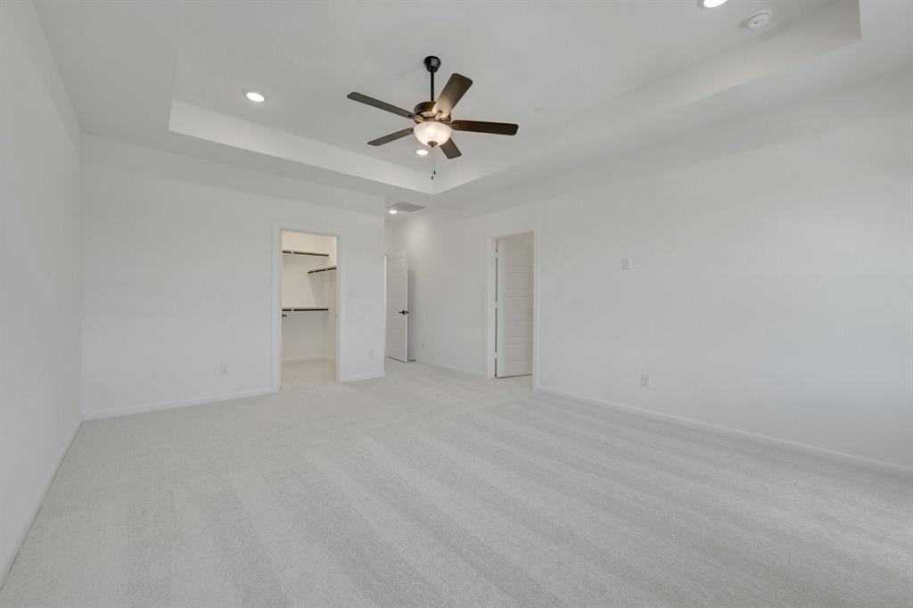 Spacious room featuring light-toned carpet, a tray ceiling with recessed lighting, and a dark-finished ceiling fan