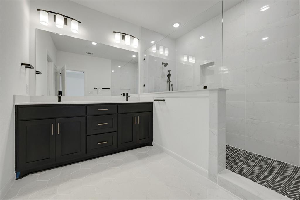 Contemporary bathroom featuring a dark wood double vanity with white countertops, expansive wall-mounted mirror, and a spacious walk-in shower with white tile walls and a patterned floor