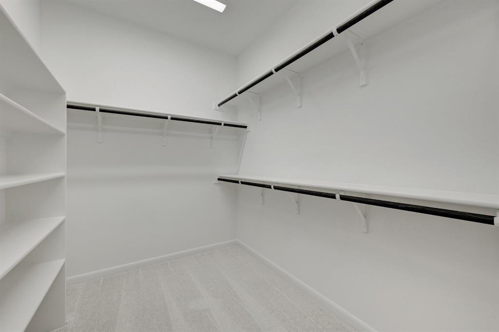 Spacious walk-in closet featuring built-in shelving, multiple hanging rods, light-colored carpet, and recessed ceiling lighting