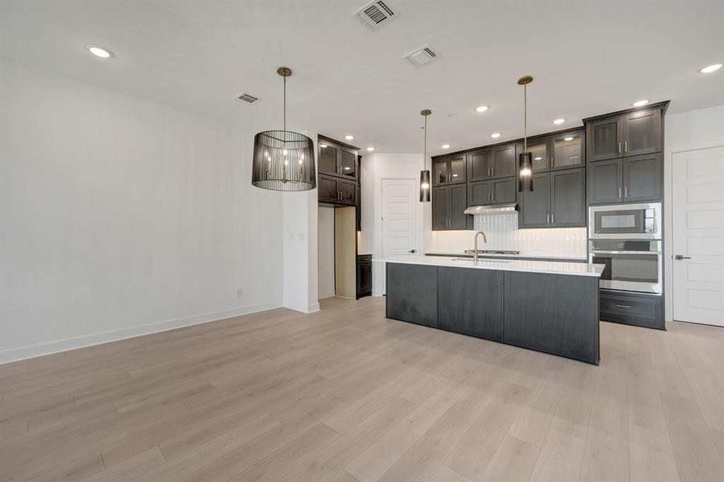 Modern kitchen featuring an island with a white countertop, dark cabinetry, and integrated stainless steel appliances