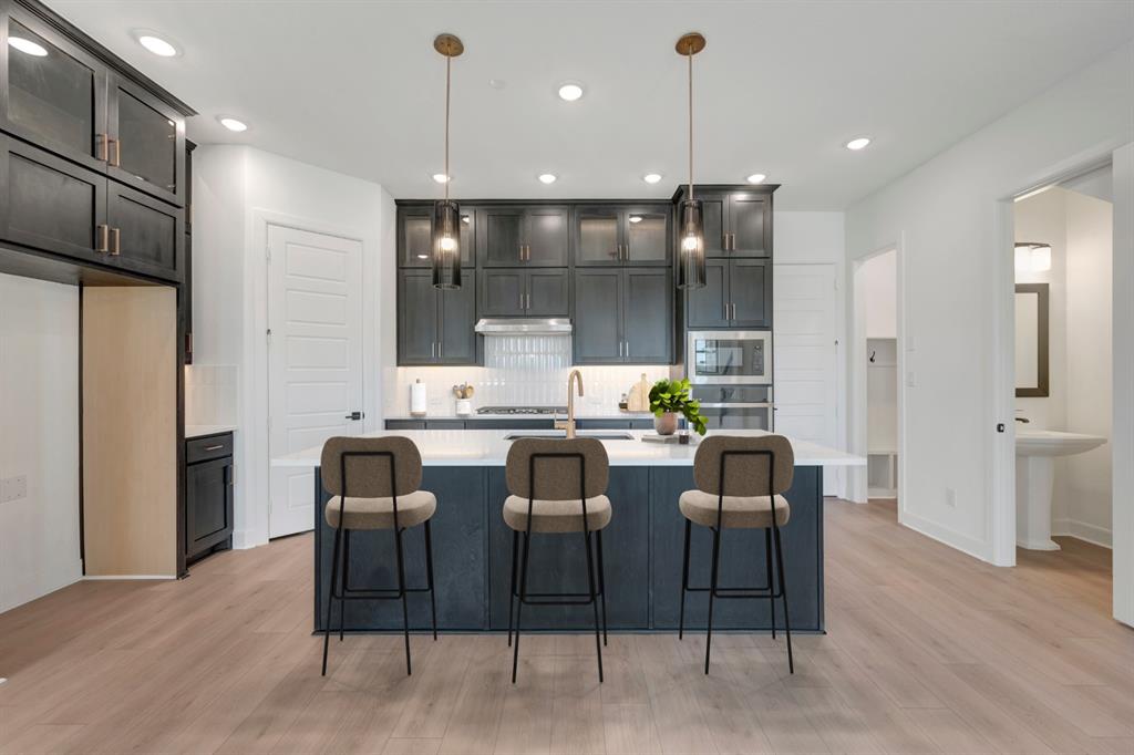 Modern kitchen featuring a central island with seating, dark shaker cabinetry, stainless steel appliances, and wood-finish flooring