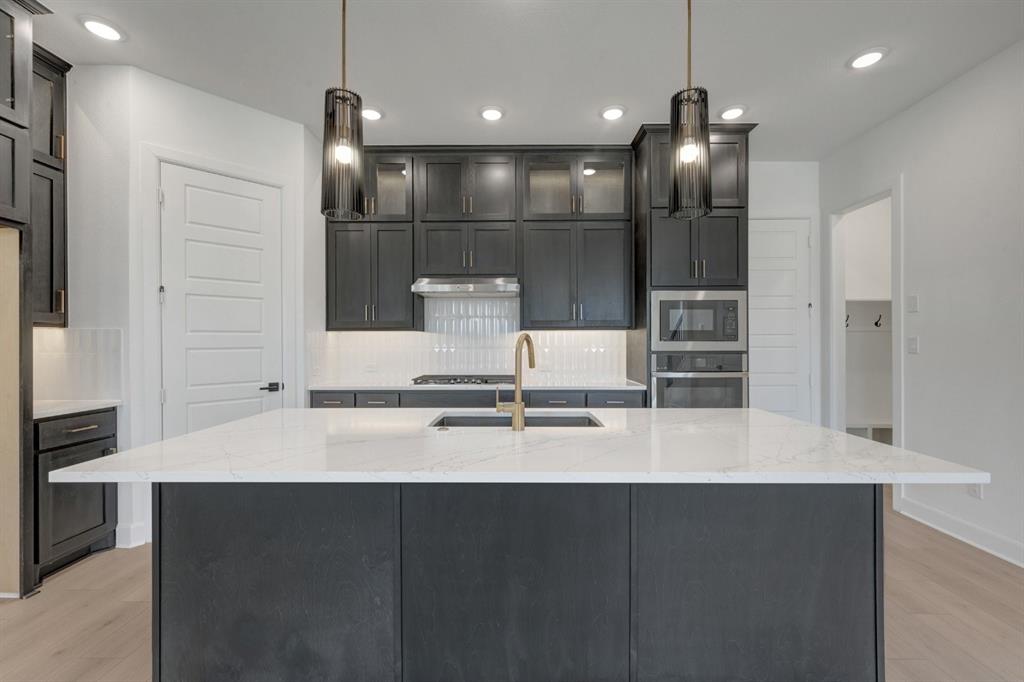 Kitchen featuring dark cabinetry, a large center island with a white stone countertop, a gold-finish faucet, and stainless steel appliances