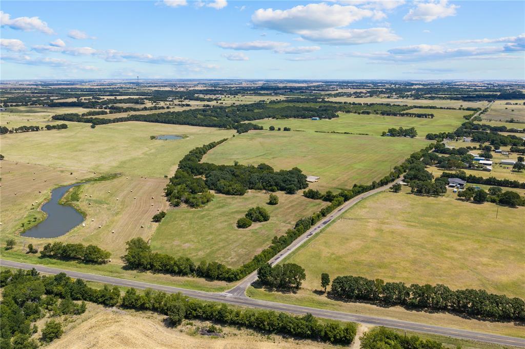 Expansive acreage featuring multiple pastures, two water features, and established tree lines along a paved road