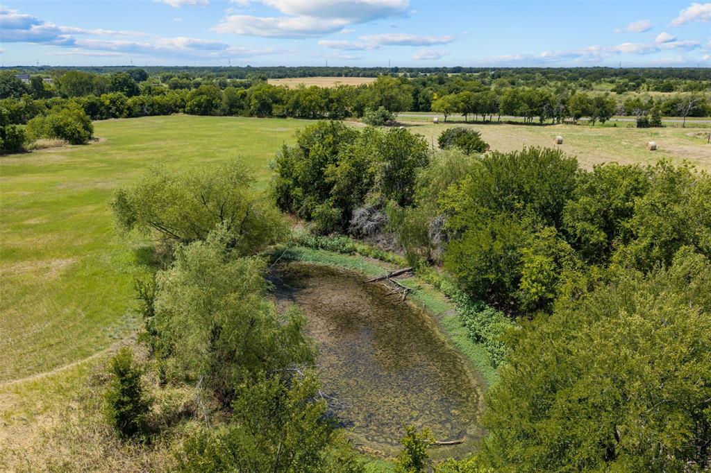 Expansive green acreage featuring a pond surrounded by lush trees