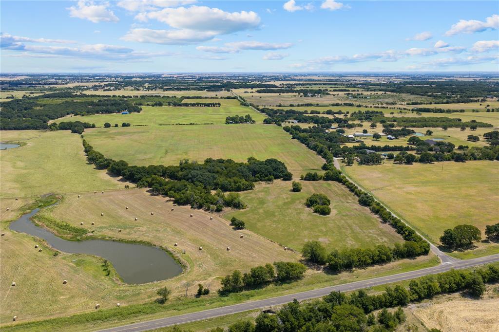 Expansive agricultural land featuring a natural pond, scattered hay bales, mature trees, and a paved road frontage Expansive agricultural land featuring a natural pond, scattered hay bales, mature trees, and a paved road frontage