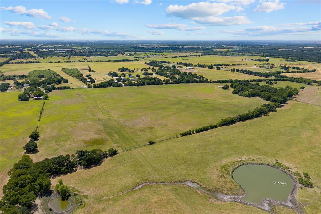 Expansive green pastureland with multiple ponds, scattered mature trees, and distant structures Expansive green pastureland with multiple ponds, scattered mature trees, and distant structures