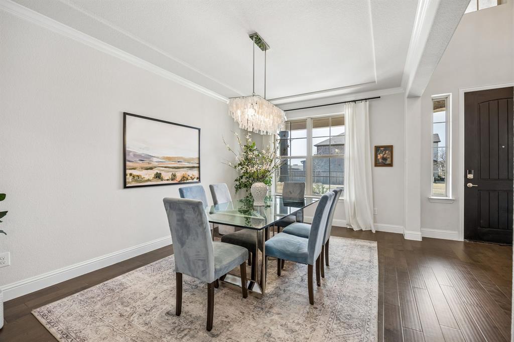 Dining space with suspended lighting, ornamental molding, and dark wood-style floors