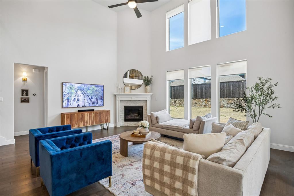 Living room with dark wood finished floors, healthy amount of natural light, a stone fireplace, and a high ceiling