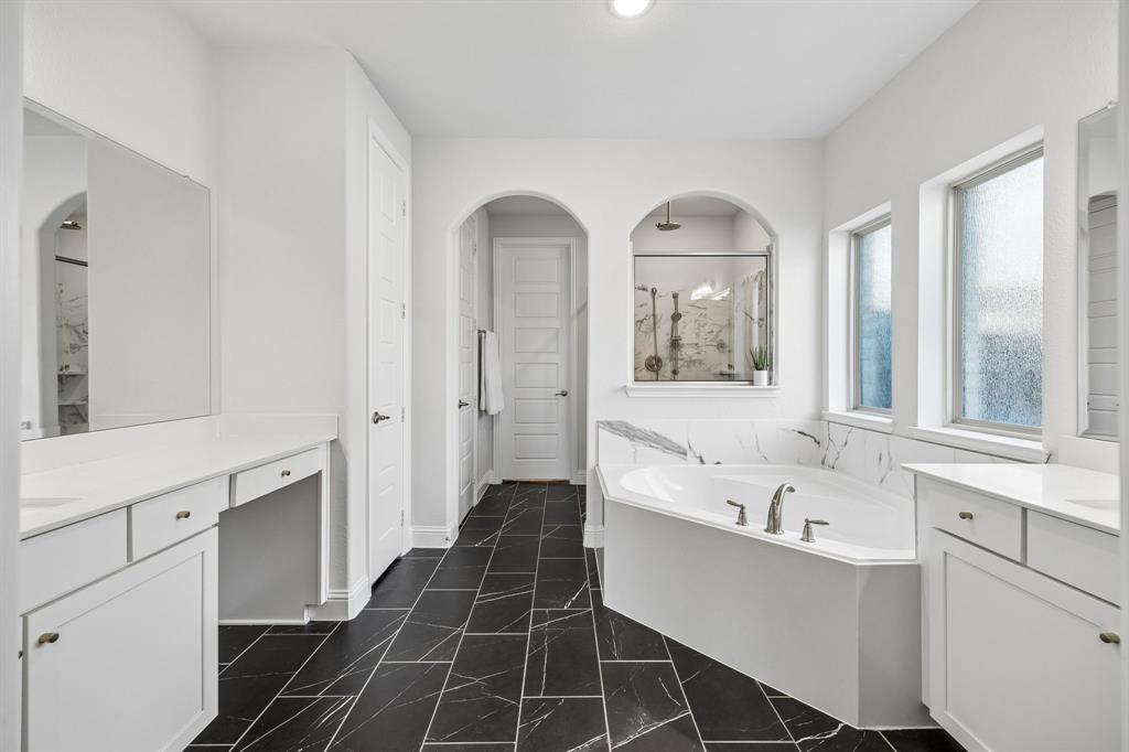 Full bathroom featuring two vanities, a garden tub, a marble finish shower, and dark marble finish floors. Walk-in Closet is connected to Utility room