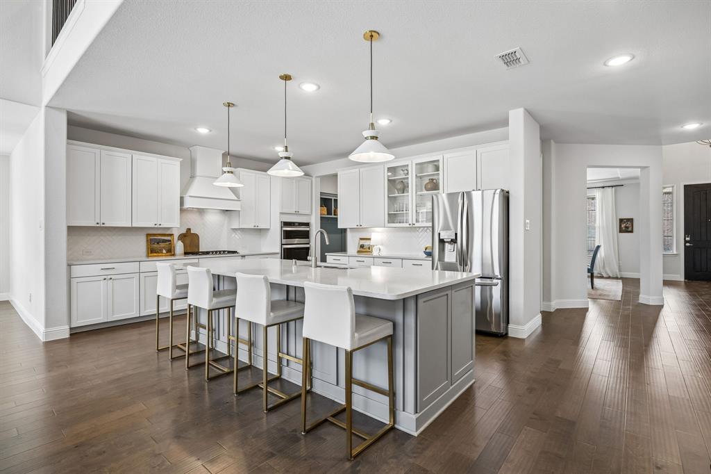 Two tone kitchen with a spacious island, stainless steel appliances, glass insert cabinets, a breakfast bar, and dark wood-type flooring