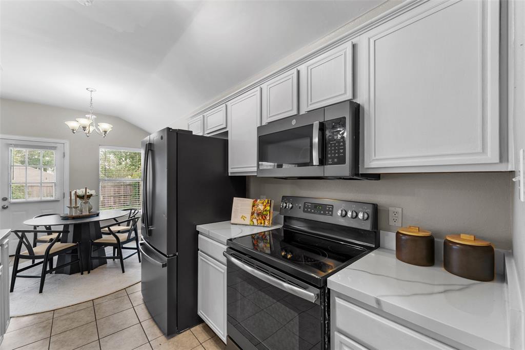 Kitchen featuring stainless steel appliances, lofted ceiling, suspended lighting, light tile patterned flooring, and light stone counters