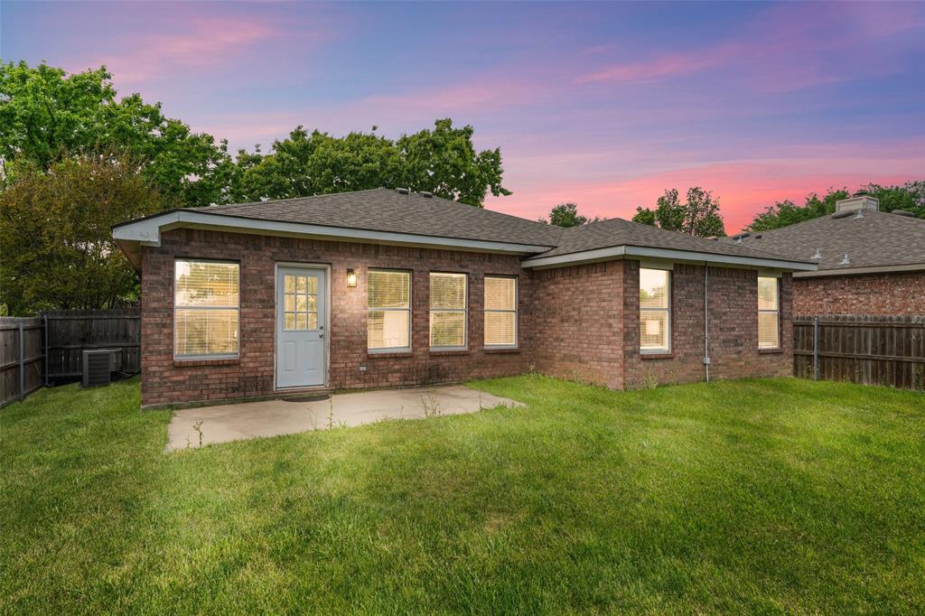 Back of property at dusk featuring a fenced backyard, brick siding, a patio, and roof with shingles