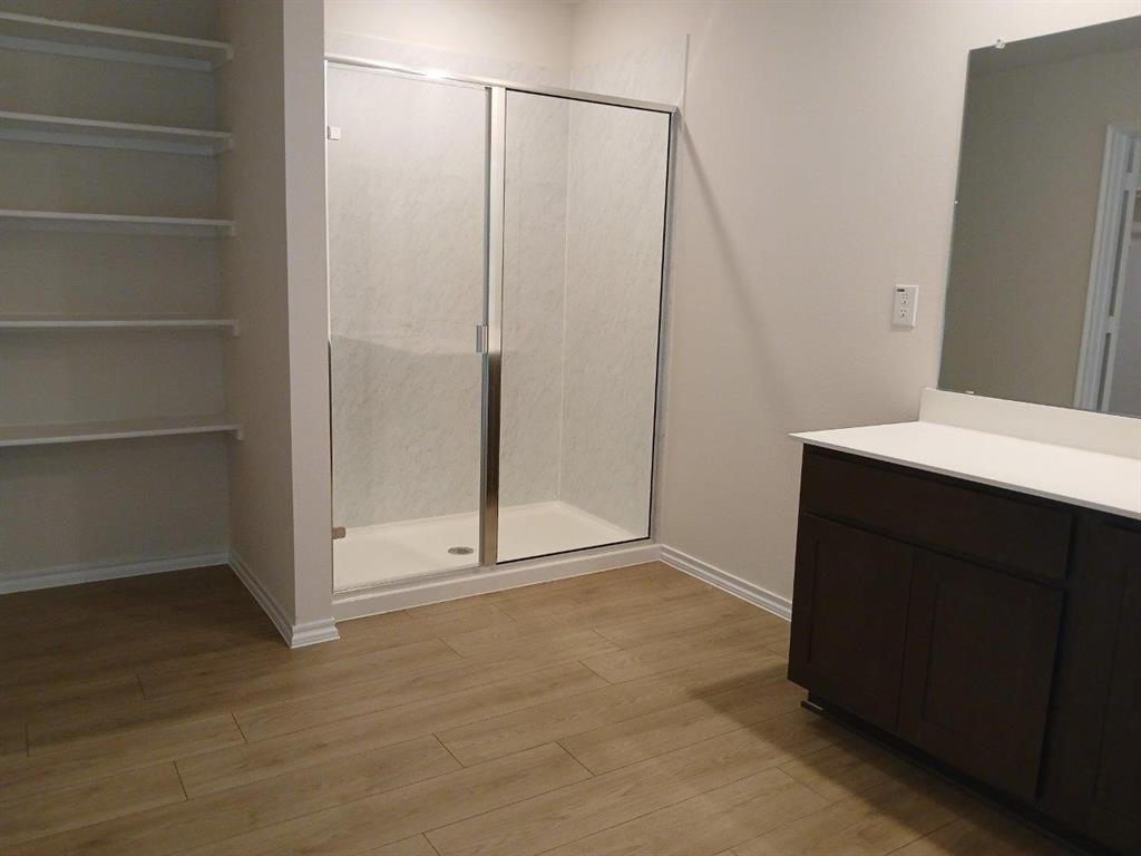 Bathroom featuring a glass-enclosed shower, wood-finish flooring, built-in shelving, a dark wood-finish vanity with a light-toned countertop, and a wall-mounted mirror