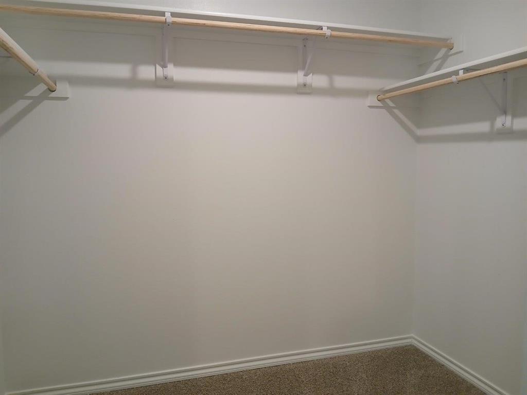 Spacious closet featuring multiple wood closet rods on white shelving brackets, light-colored carpeting, and white baseboard trim
