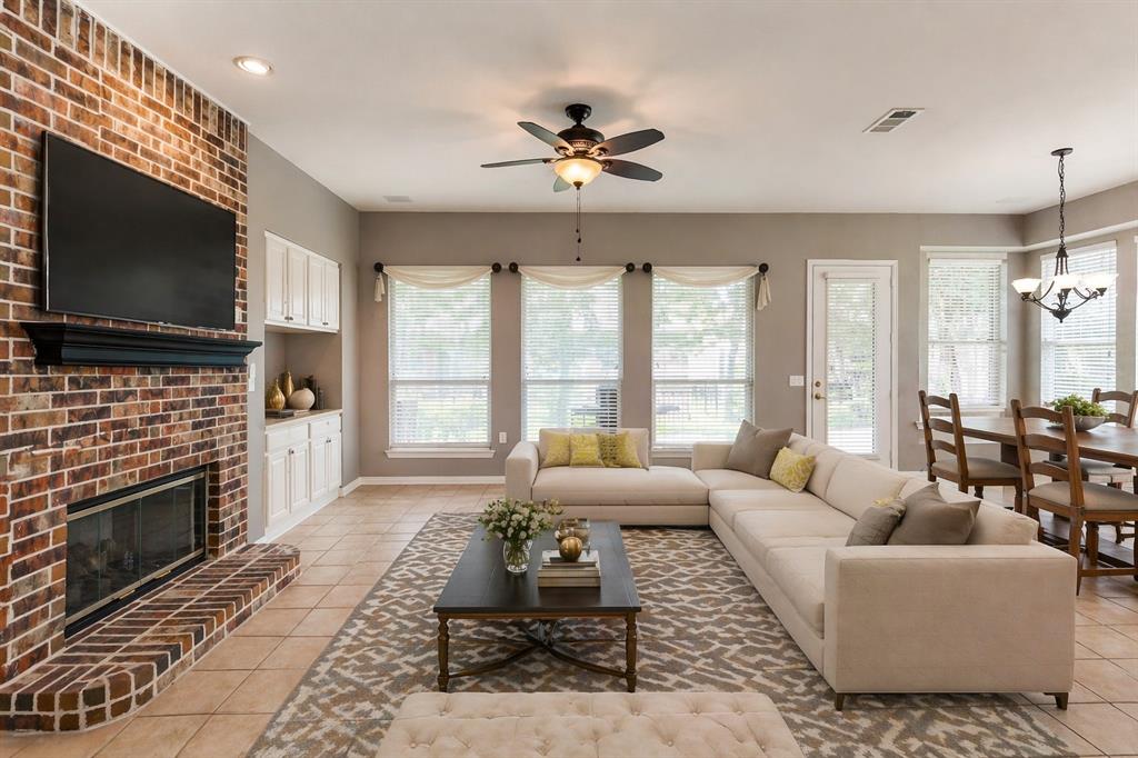 Spacious living area featuring a brick fireplace, built-in cabinetry, tile flooring, a ceiling fan, and ample natural light through multiple windows - Virtually Staged