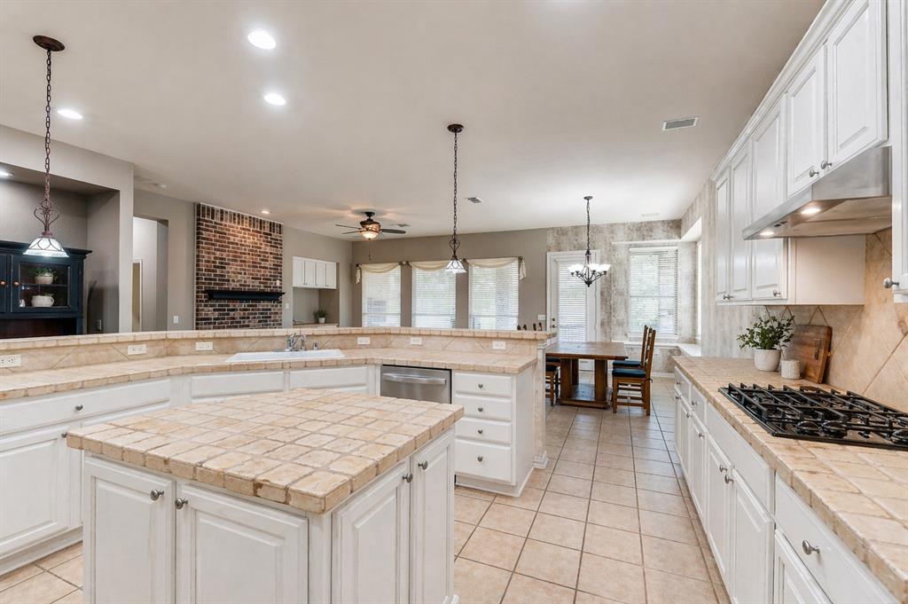 Spacious kitchen featuring white cabinetry, tile countertops, a center island, a gas cooktop, and an integrated dishwasher