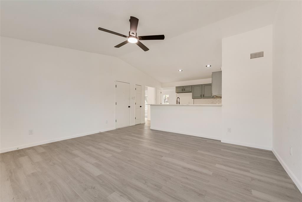 Unfurnished living room featuring a ceiling fan, vaulted ceiling, and light wood-style flooring