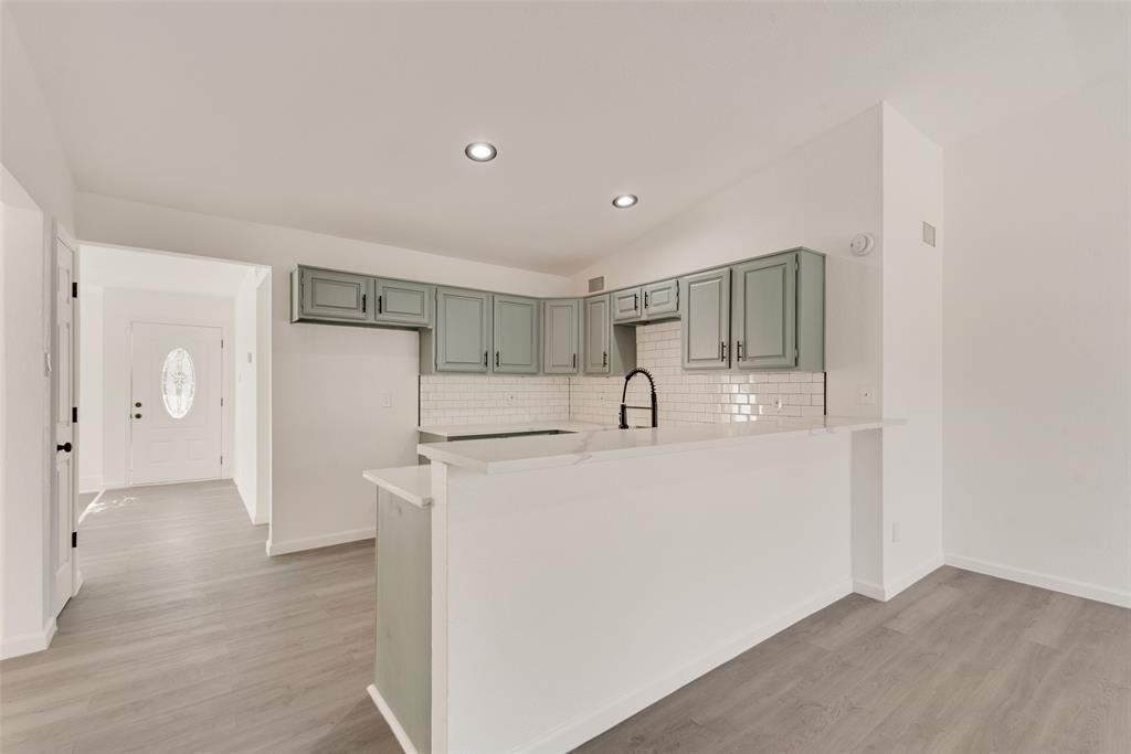Kitchen featuring a peninsula, lofted ceiling, light wood-style floors, backsplash, and a breakfast bar area