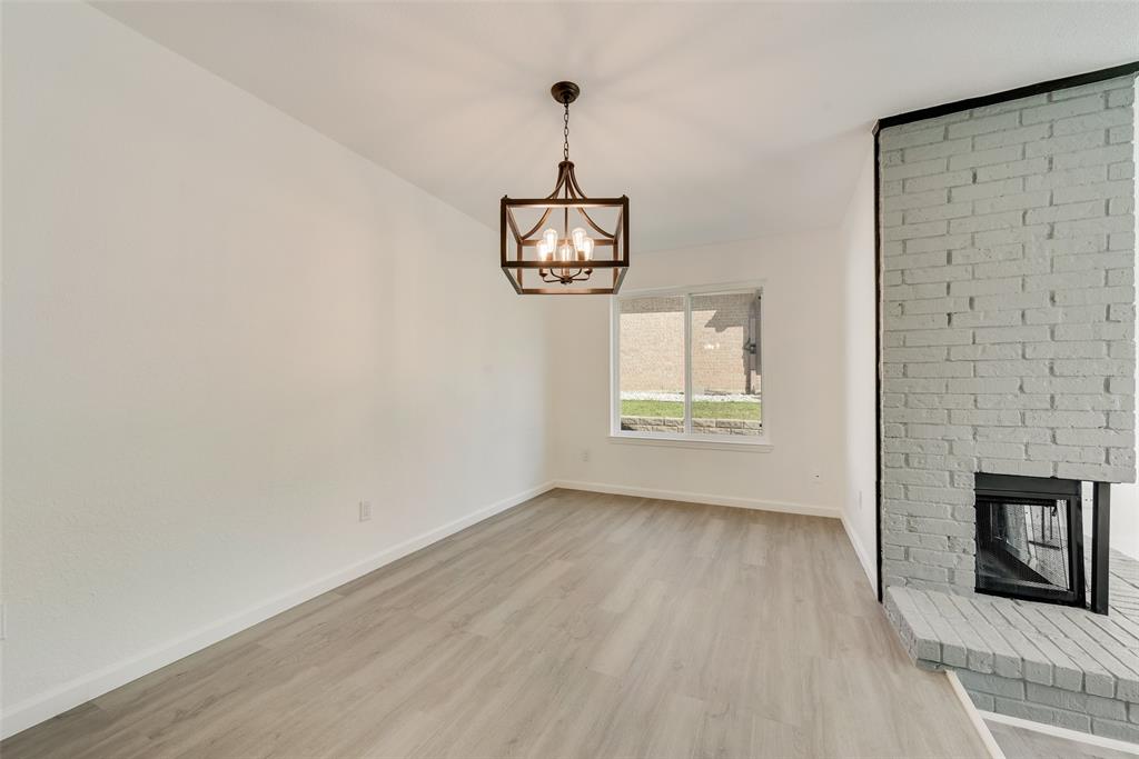 Unfurnished dining room featuring light wood-type flooring, a brick fireplace, and suspended lighting
