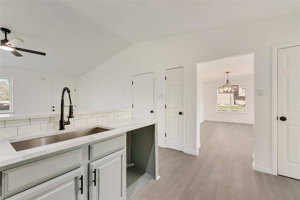 Kitchen with light stone countertops, plenty of natural light, light wood-type flooring, ceiling fan, and vaulted ceiling