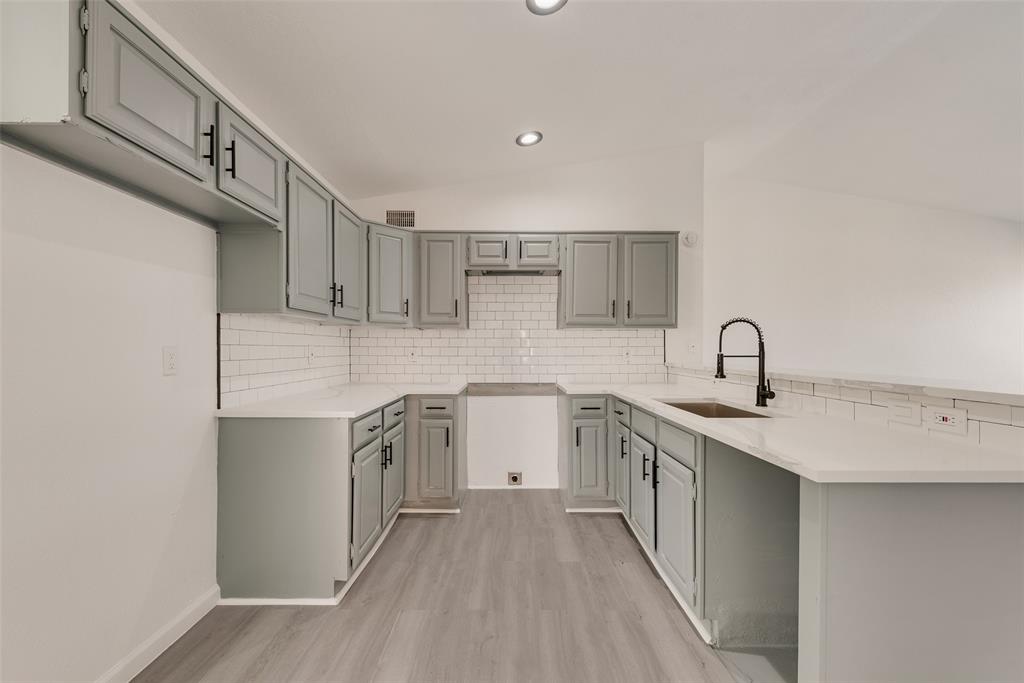 Kitchen with a peninsula, vaulted ceiling, light wood finished floors, light stone countertops, and decorative backsplash Kitchen with a peninsula, vaulted ceiling, light wood finished floors, light stone countertops, and decorative backsplash