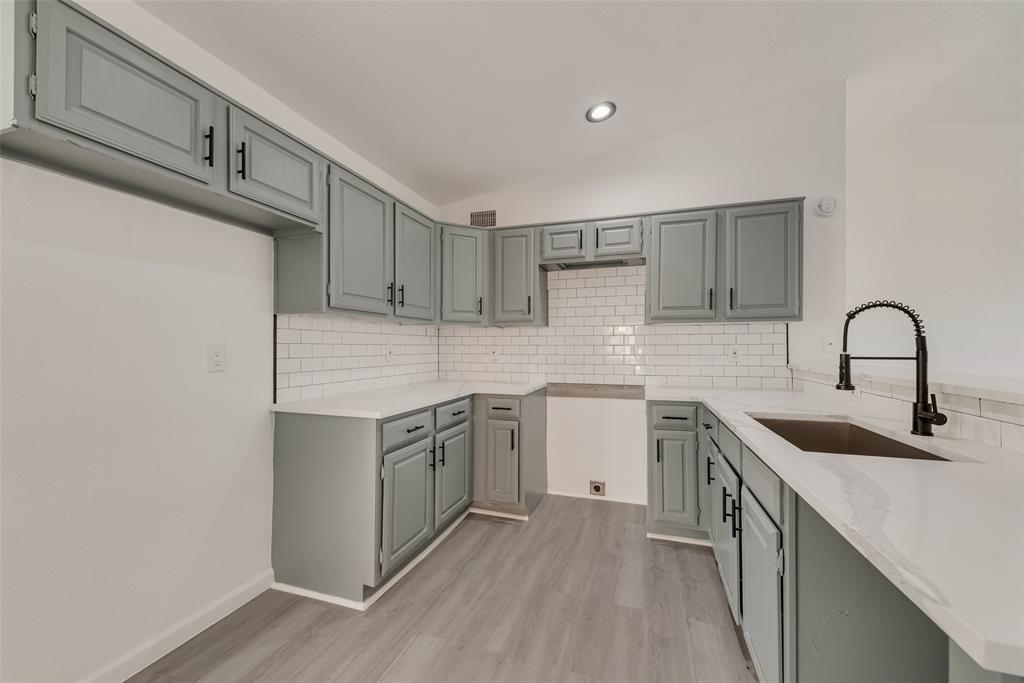 Kitchen featuring lofted ceiling, light stone counters, light wood finished floors, a peninsula, and gray cabinetry