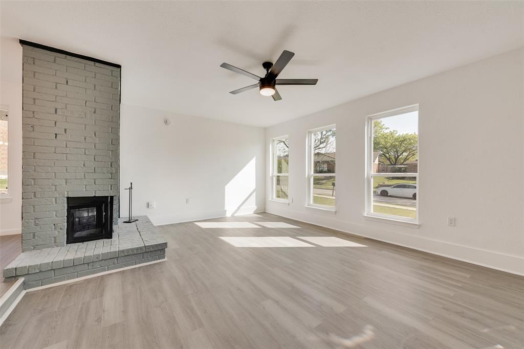 Unfurnished living room featuring a brick fireplace, light wood finished floors, and a ceiling fan Unfurnished living room featuring a brick fireplace, light wood finished floors, and a ceiling fan
