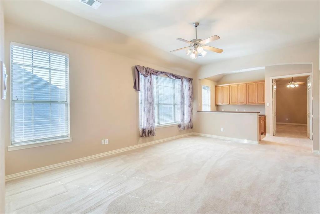 Open-concept living area featuring light-toned carpeting, multiple windows with blinds, a ceiling fan with integrated lighting, and a breakfast bar with built-in cabinetry