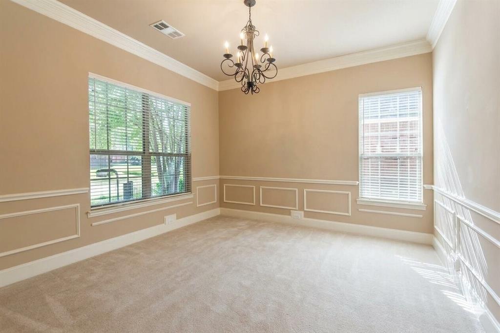 Spacious room featuring neutral carpeting, decorative wainscoting, crown molding, and an ornate wrought-iron chandelier