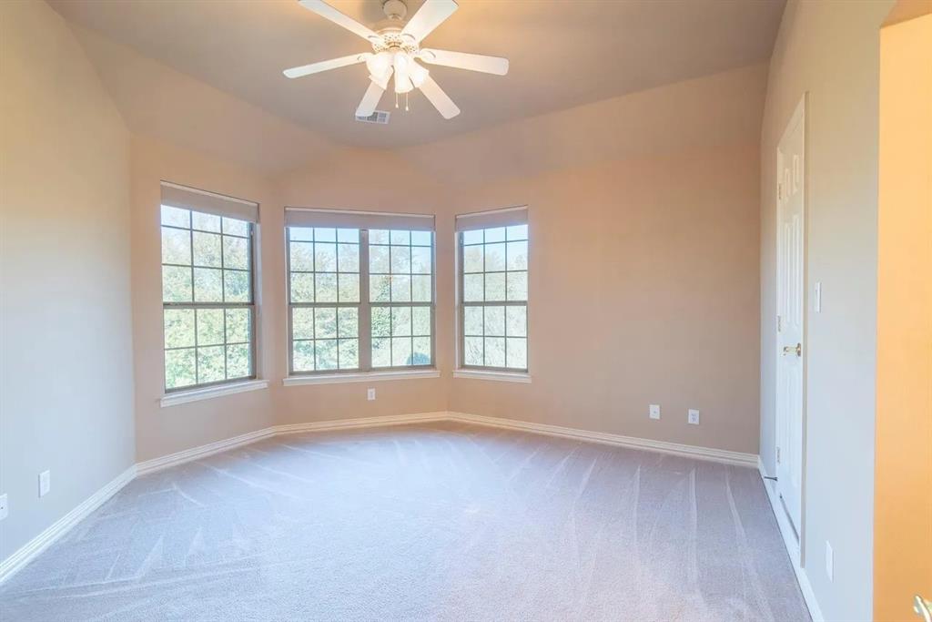 Spacious room featuring a bay window with three large windows, a vaulted ceiling, a ceiling fan, plush carpeting, and neutral paint tones