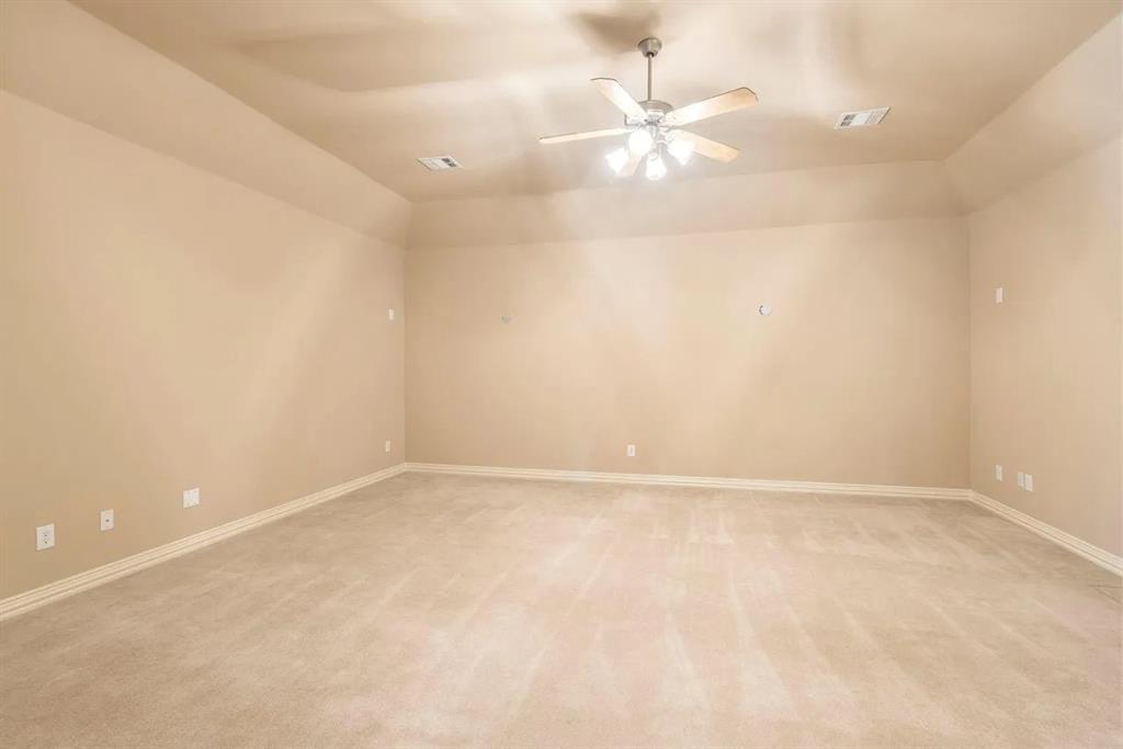 Spacious room featuring neutral carpeting, light beige wall paint, a tray ceiling, and a ceiling fan with integrated lighting