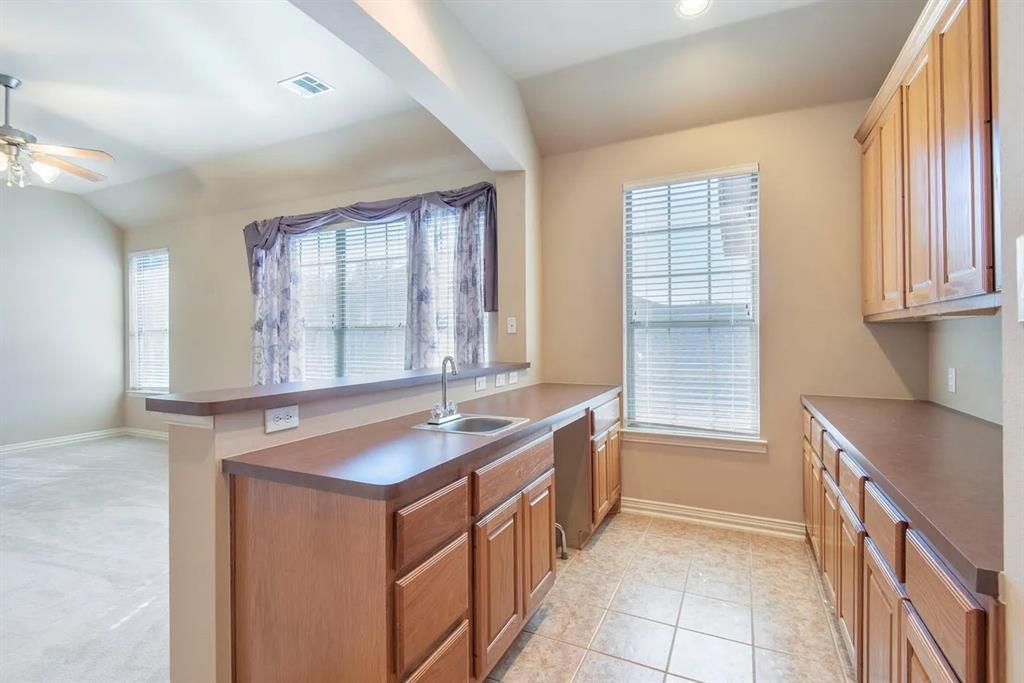 Kitchenette featuring wood-finish cabinetry, a built-in sink, and tile flooring