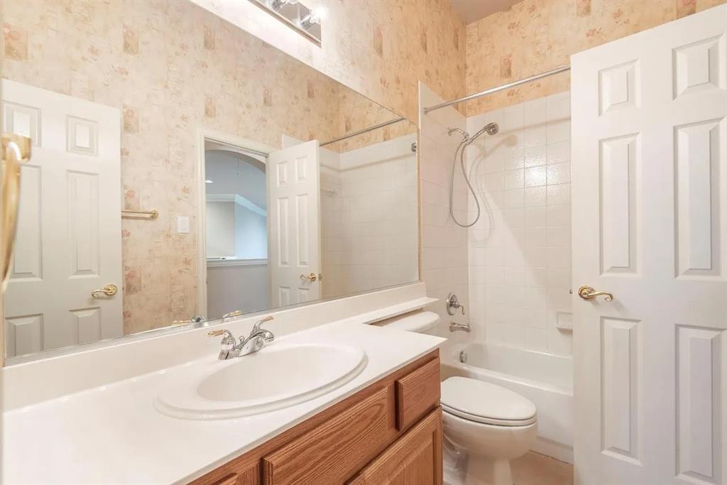 Full bathroom featuring a single-sink vanity with a white countertop and wood-finish cabinetry, a built-in tub with white tile surround, and two panel doors