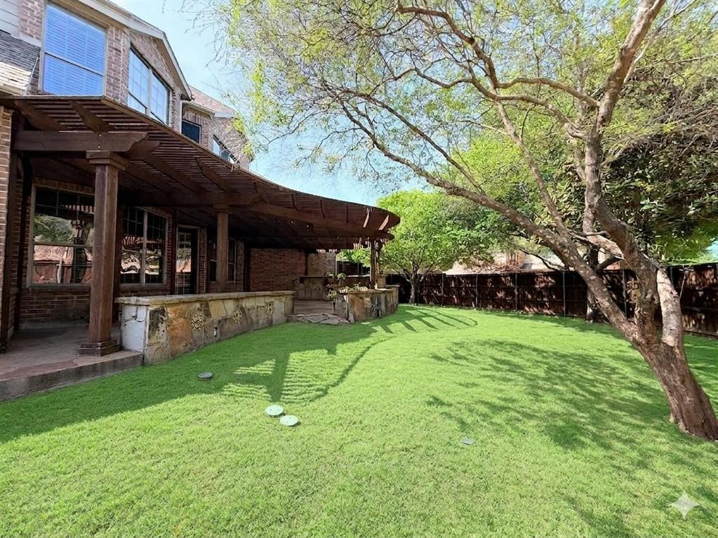 Spacious backyard featuring a manicured lawn, established shade trees, and a wooden pergola covering a stone patio