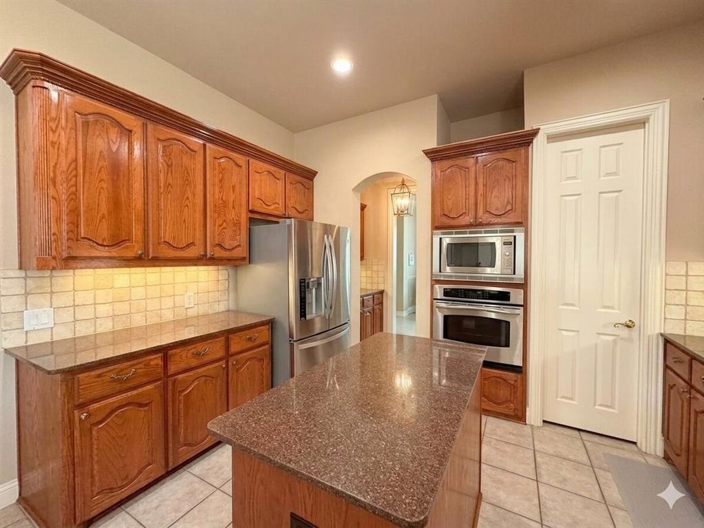 Kitchen featuring wood cabinetry, stainless steel appliances, a center island with a stone-finish countertop, and tile flooring
