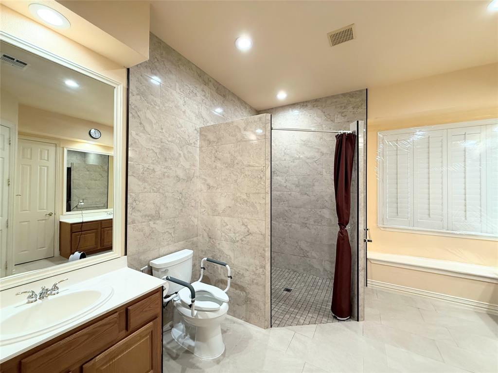 Bathroom featuring a walk-in shower with tile walls, a vanity with a white countertop, and a window with white shutters