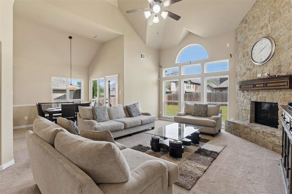 Living room featuring light carpet, a stone fireplace, ceiling fan, and vaulted ceiling
