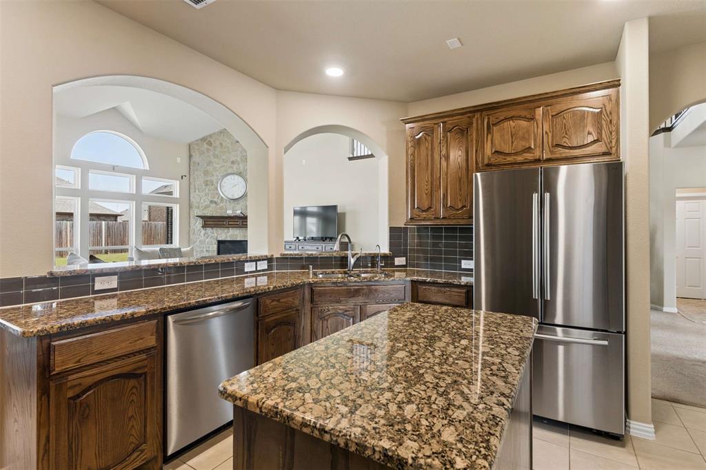 Kitchen with stainless steel appliances, dark stone countertops, a fireplace, backsplash, and light tile patterned flooring