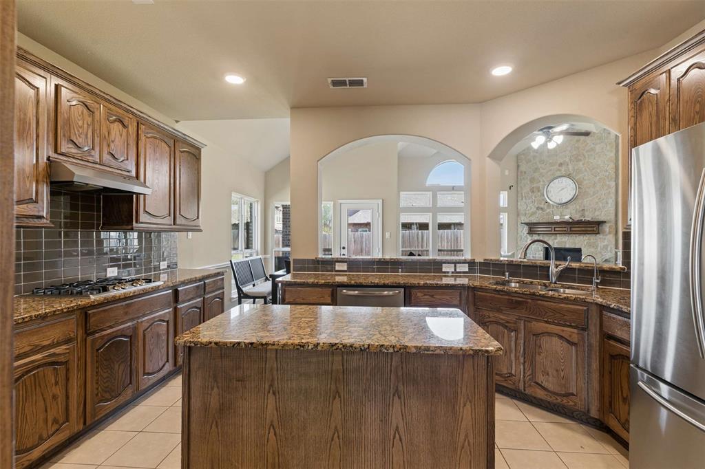 Kitchen with decorative backsplash, a center island, dark stone counters, a stone fireplace, and recessed lighting