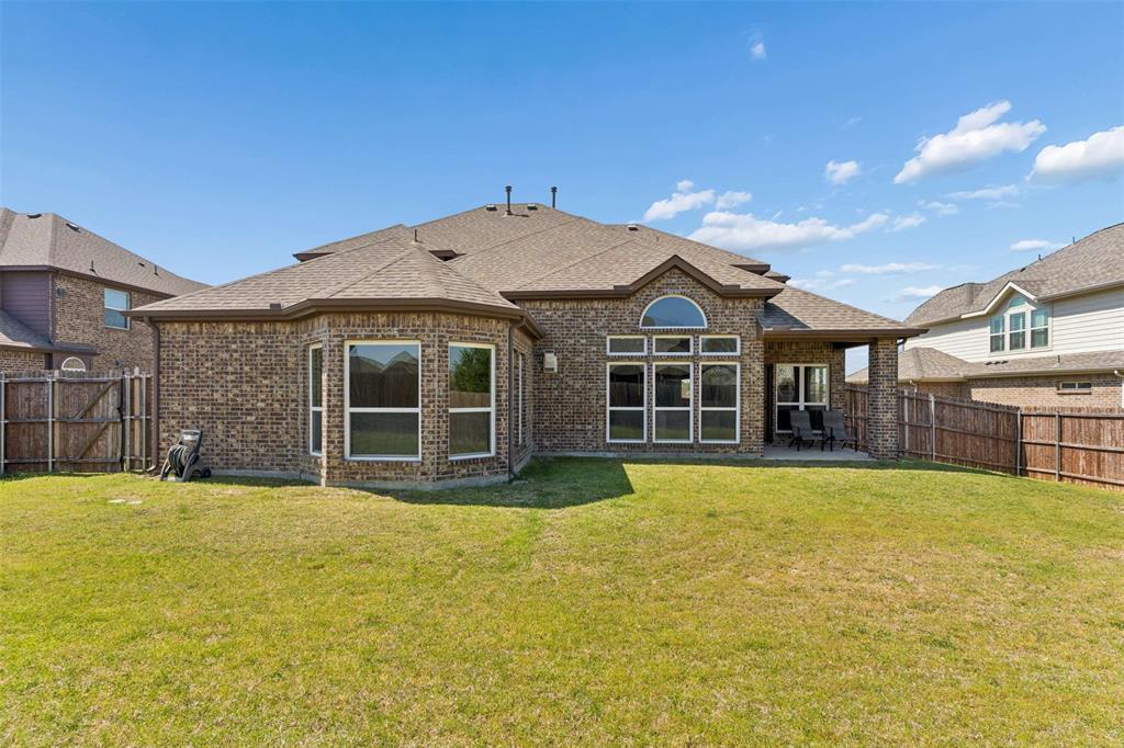 Rear view of house featuring brick siding, a shingled roof, a fenced backyard, and a patio