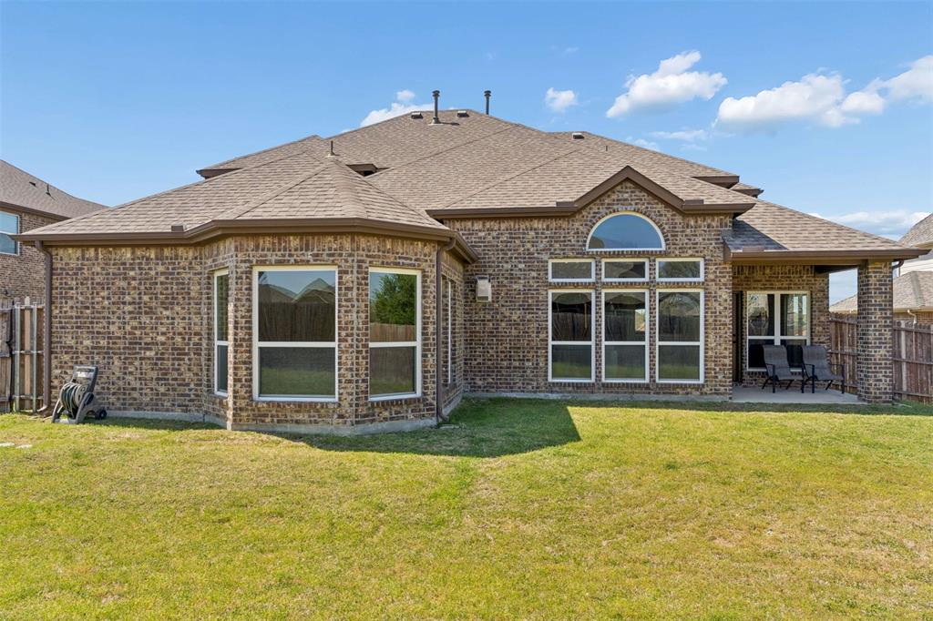 Rear view of property with a fenced backyard, brick siding, roof with shingles, and a patio area