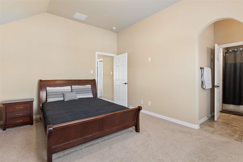 Bedroom featuring light colored carpet, arched walkways, connected bathroom, and vaulted ceiling