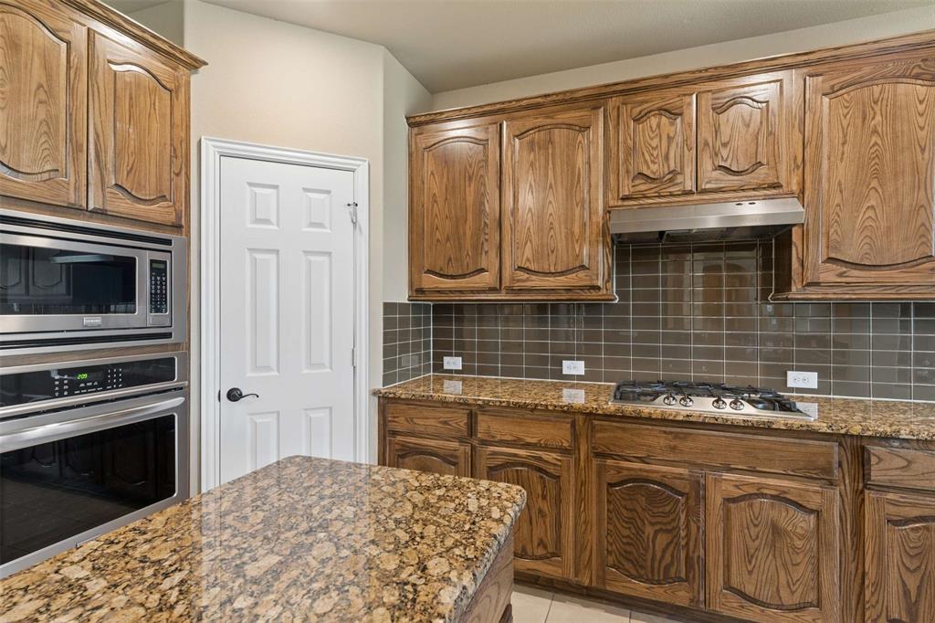 Kitchen with dark stone countertops, stainless steel appliances, wood finish cabinets, backsplash, and light tile patterned flooring
