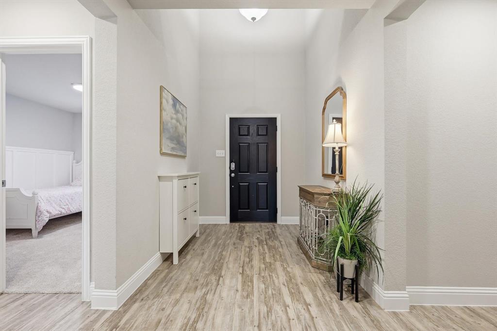 Entryway featuring wood-finish flooring, a paneled black door, vaulted ceiling, and neutral wall tones