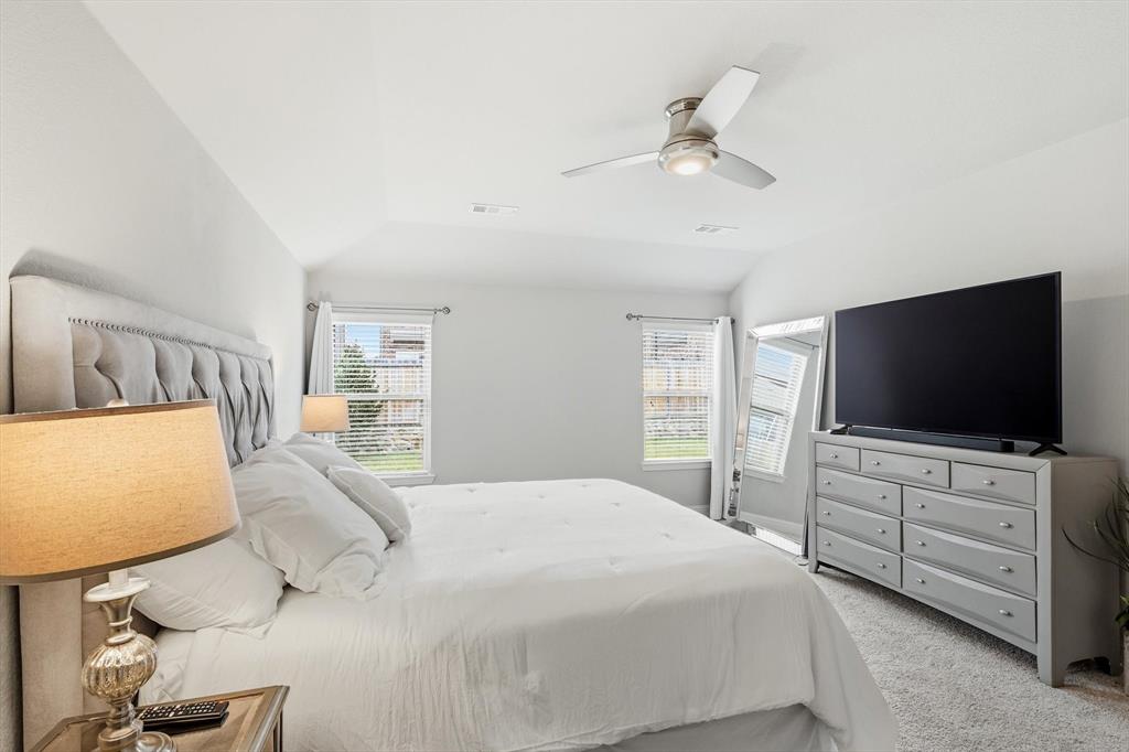 Vaulted ceiling bedroom with a ceiling fan light fixture, two windows with blinds, and plush carpeting