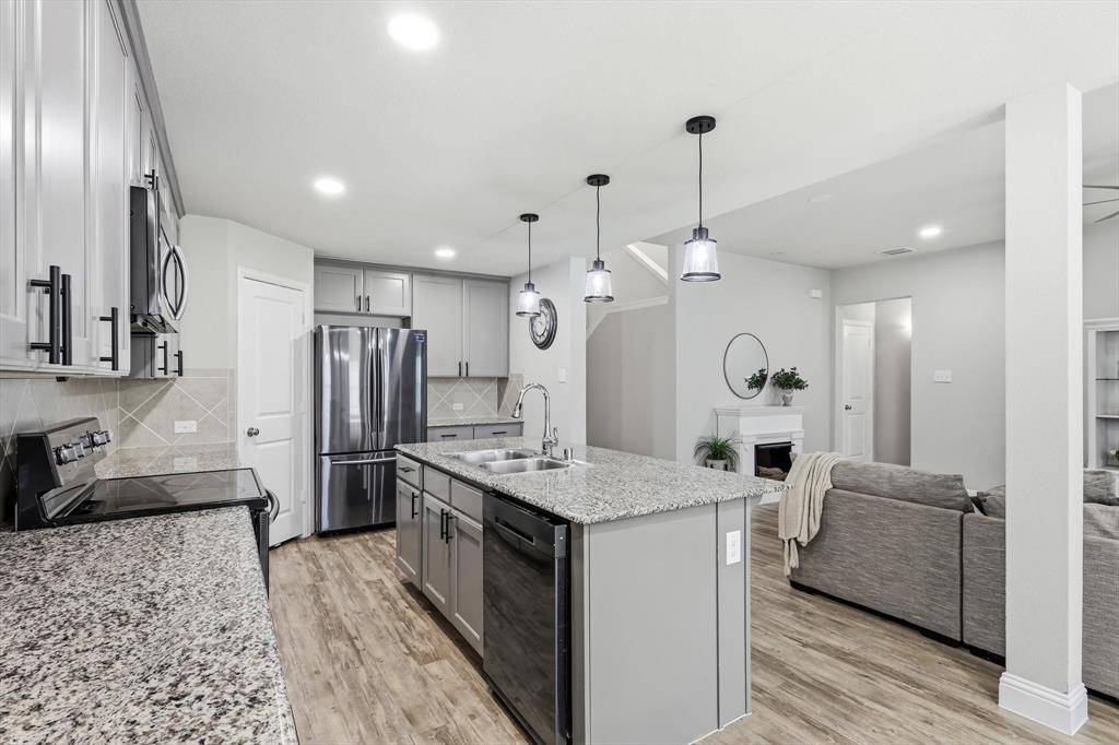 Open-concept kitchen featuring granite countertops, stainless steel appliances, a central island with pendant lighting, and wood-finish flooring